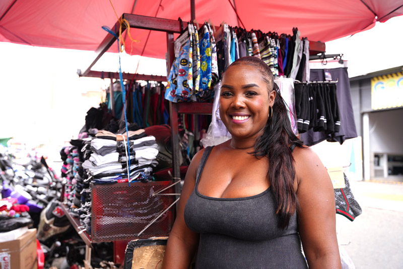 Mujer sonriente de tez morena, de pie en un puesto de mercado al aire libre que vende ropa interior y calcetines
