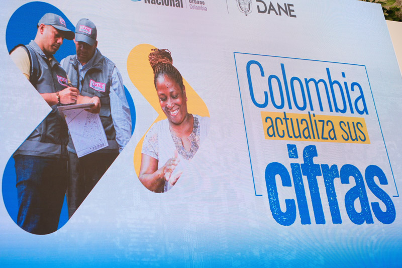 Panel informativo o pantalla con el mensaje 'Colombia actualiza sus cifras', junto a imágenes de funcionarios del DANE realizando una encuesta y el retrato de una mujer sonriente
