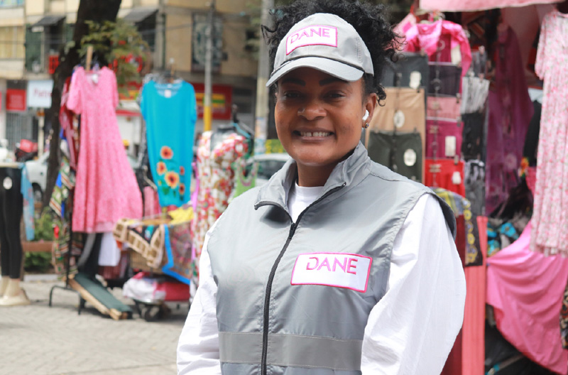 Encuestadora afro, vistiendo indumentaria del DANE. Cachucha, chaleco y morral.